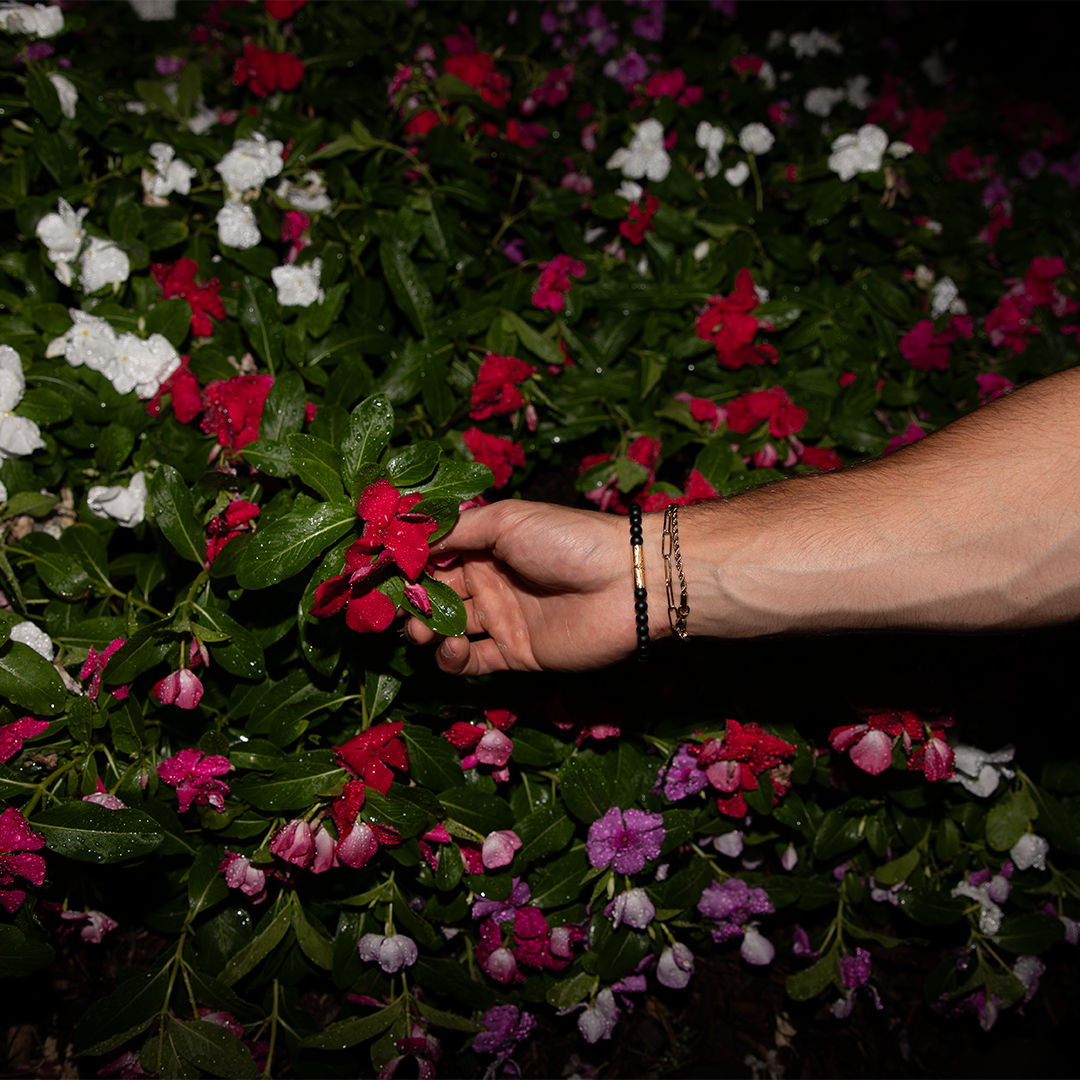 close up of farvahar Bracelet on a male model's wrist against a backdrop of red flowers
